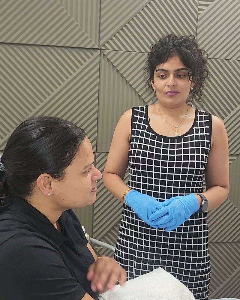 Hetisha Shukla, in gloves, standing beside a colleague in a treatment room at Oxyderm Laser Clinic